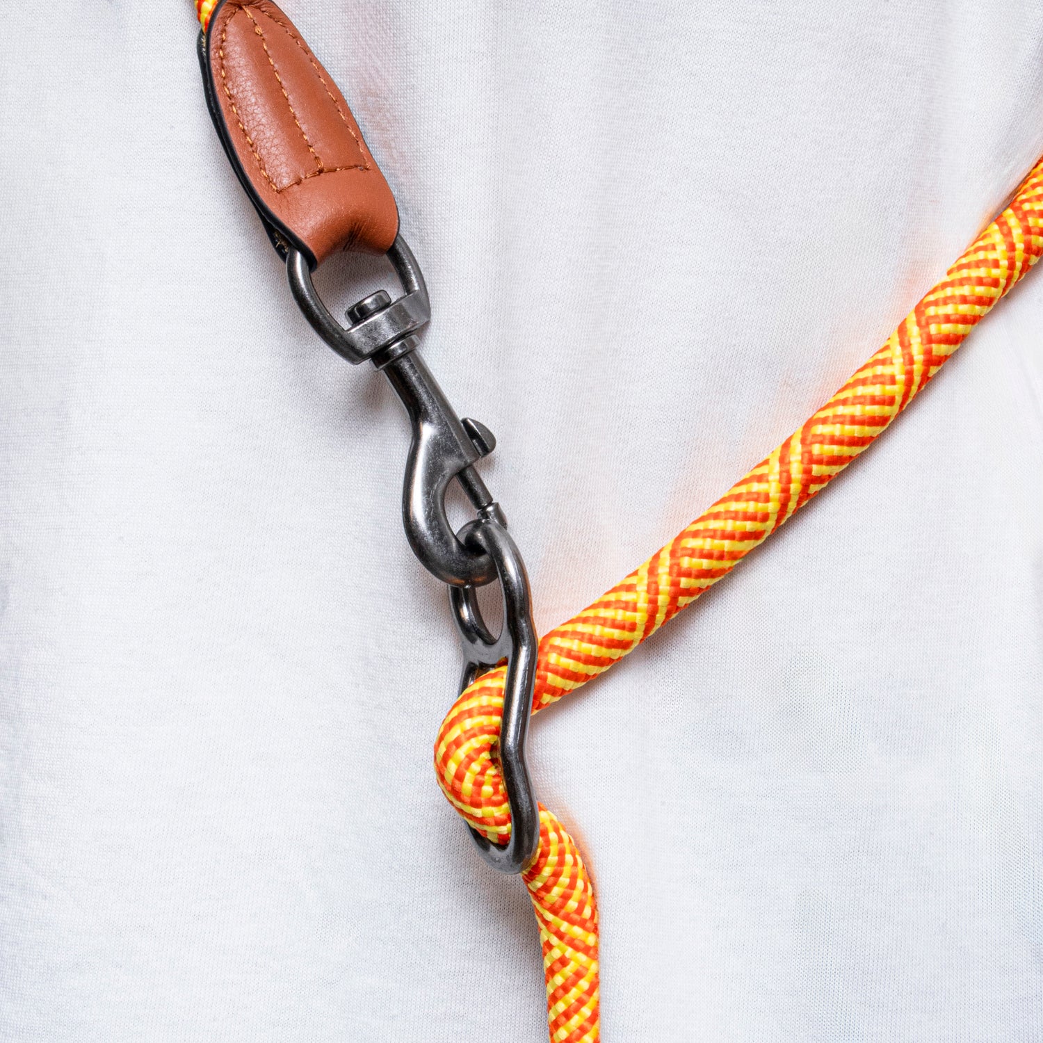 Close-up of a yellow rope dog leash with a metal clasp and brown leather handle on a white background